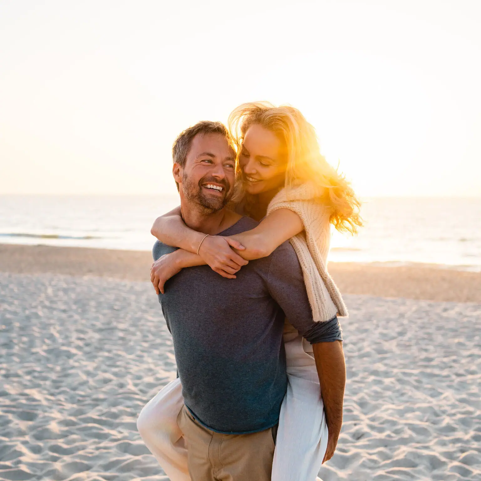 A man carrying a smiling woman on his back on a beach.