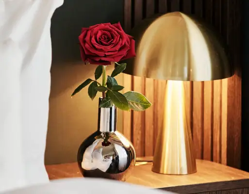 A rose in a vase next to a lamp.