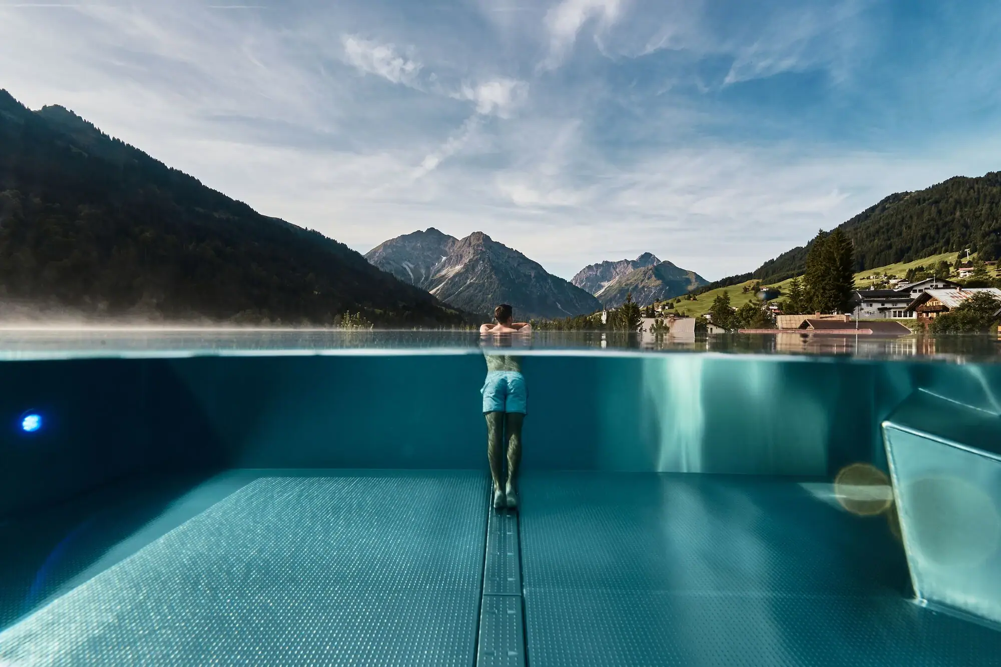 Infinity pool A person is standing in a swimming pool with mountains in the background.