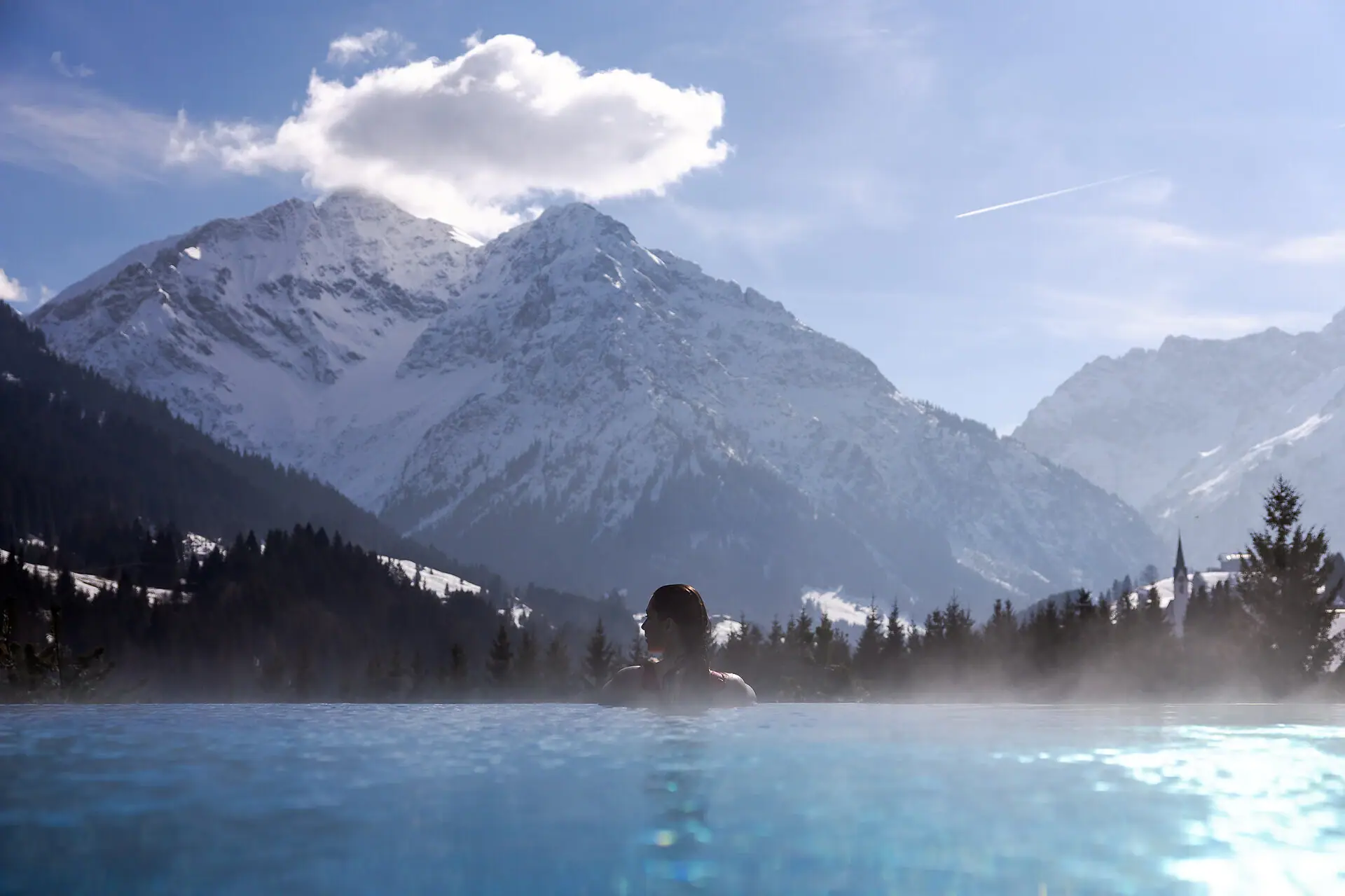 A person swimming in a pool with a mountain range in the background.