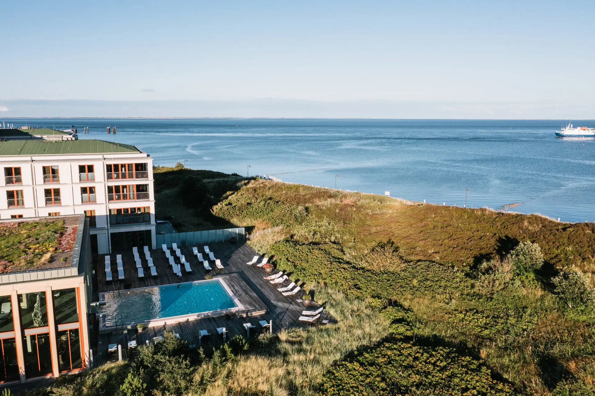 A-ROSA Sylt An outdoor pool in front of a building with a view of the sea in the background.