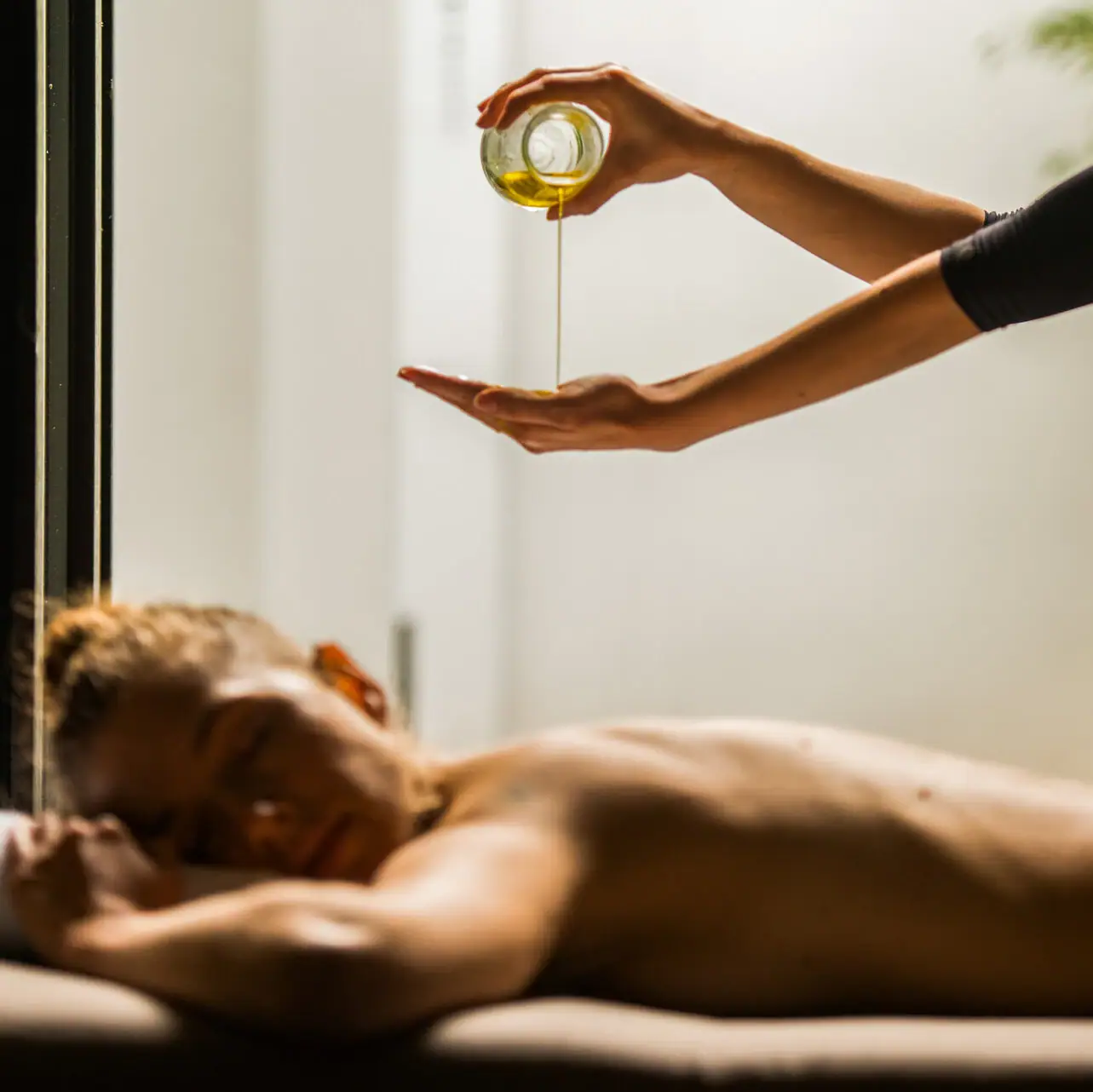 A person pouring oil into another person's hand indoors.